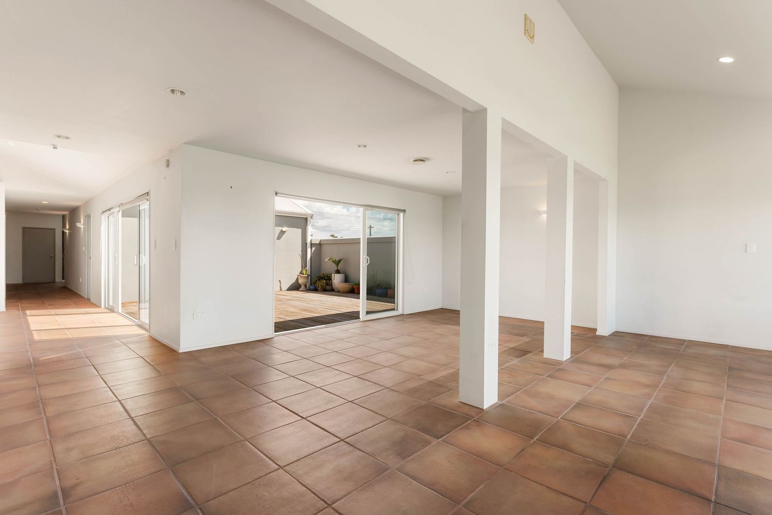 Large empty room with white walls, structural pillars and terracotta tile flooring.