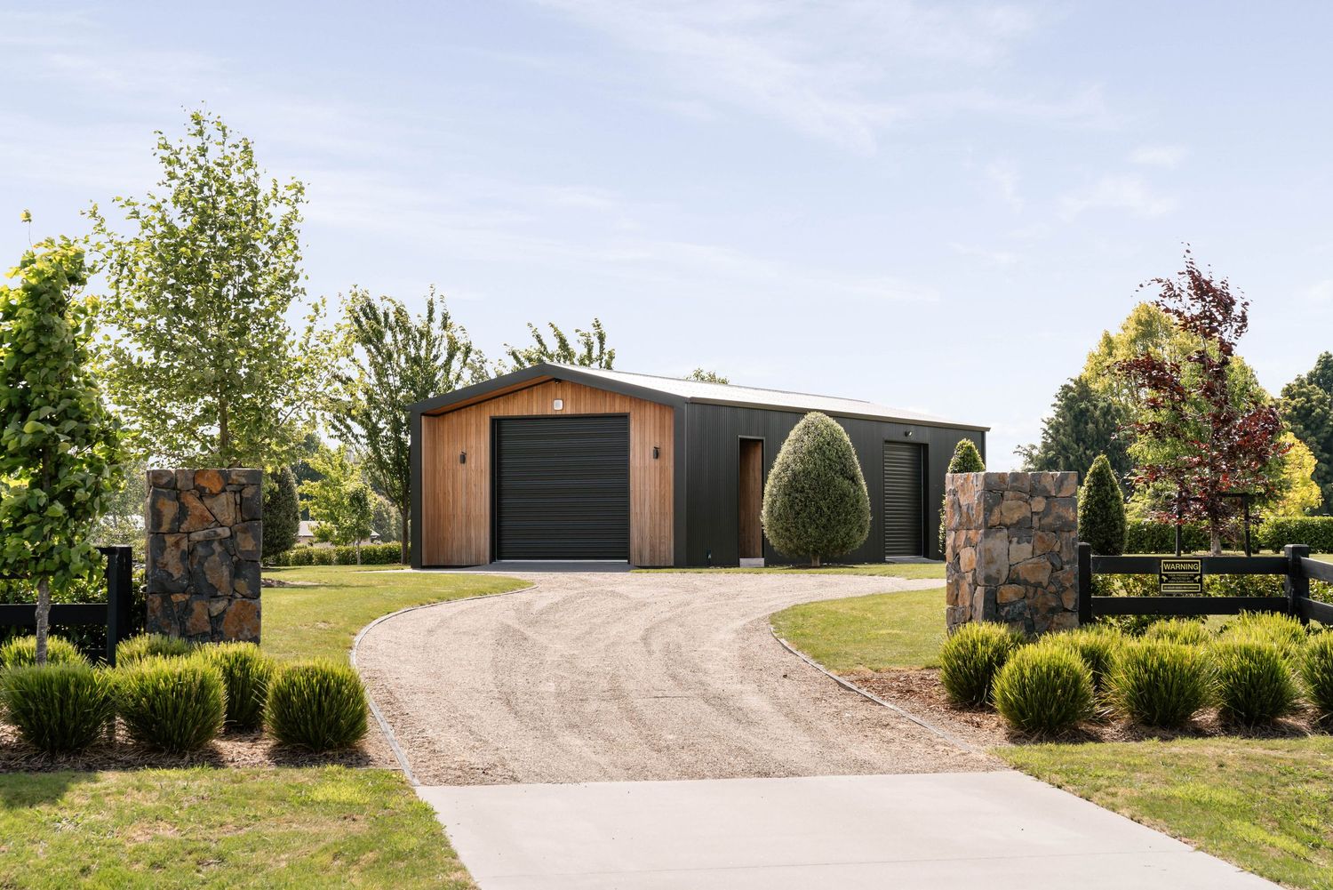 Modern dark garage building with stone pillars and curved driveway surrounded by landscaping.