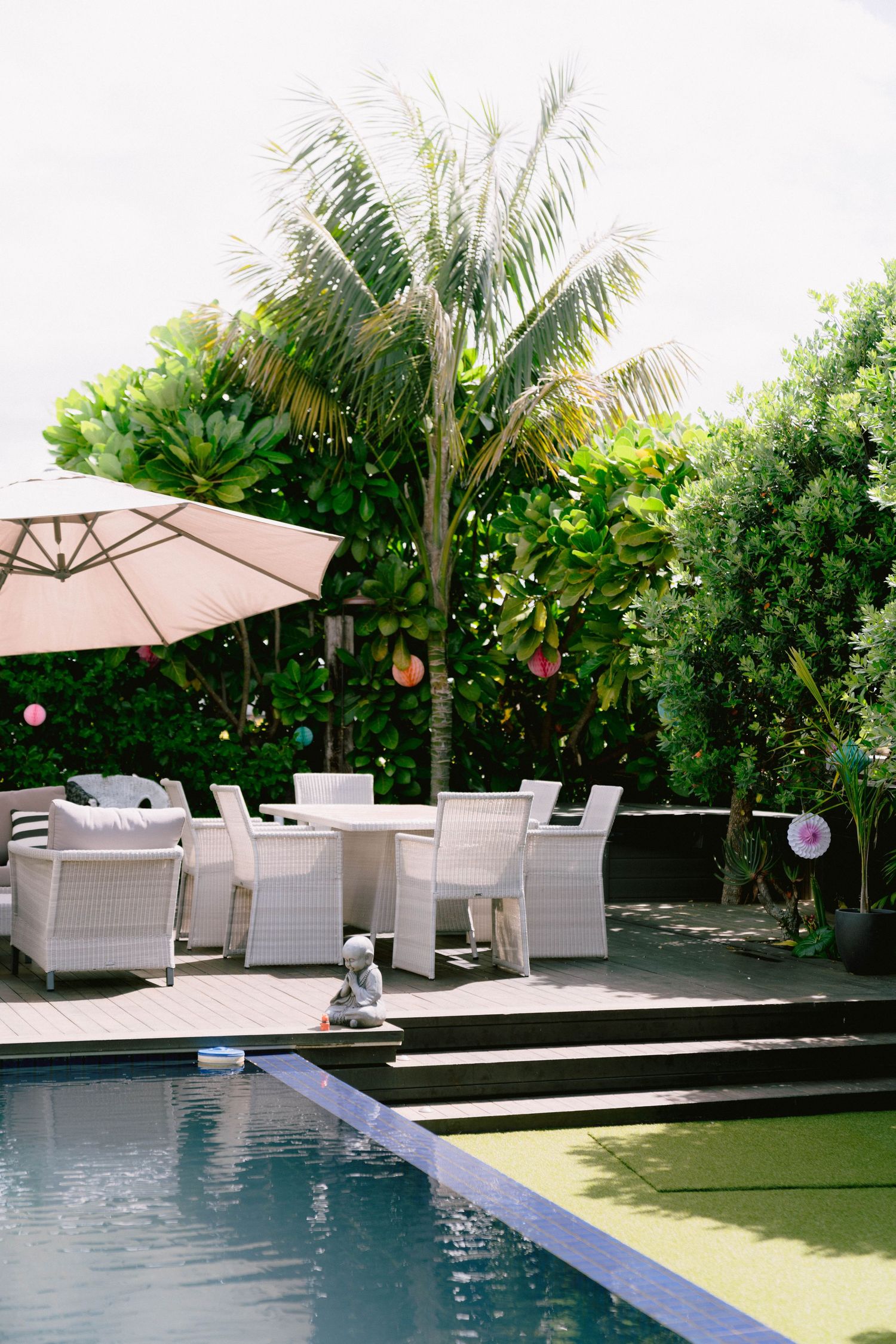 Modern outdoor patio furniture and umbrella arranged beside a swimming pool with tropical palm tree landscaping.