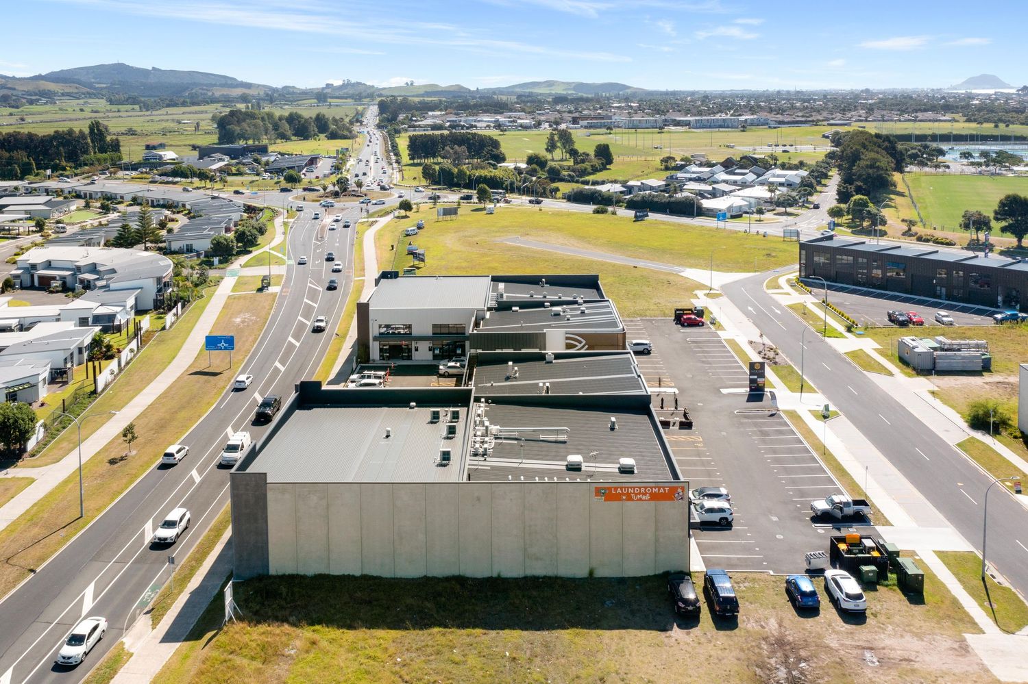 Aerial view of a commercial building complex with parking lots and roads in a suburban area surrounded by mountains.