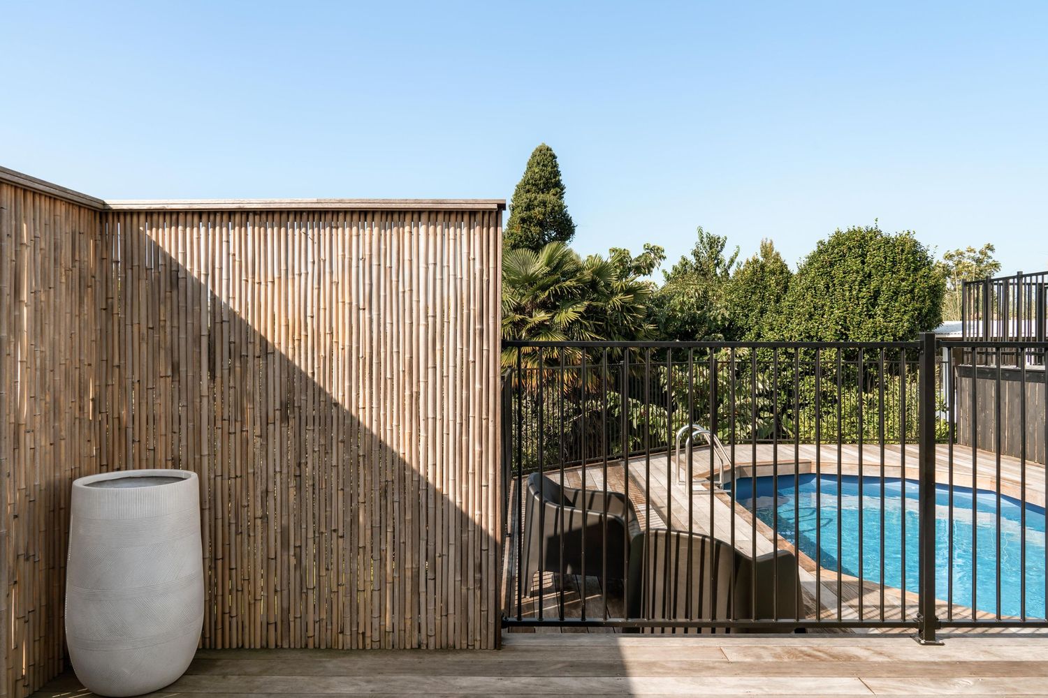 Bamboo privacy screen beside swimming pool with modern grey planter.