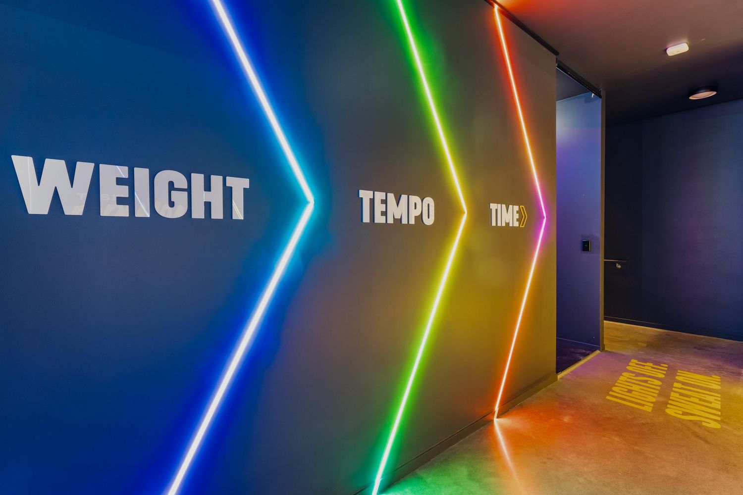 Interior hallway with colorful neon lighting displaying 'Weight', 'Tempo', and 'Time' on dark walls.