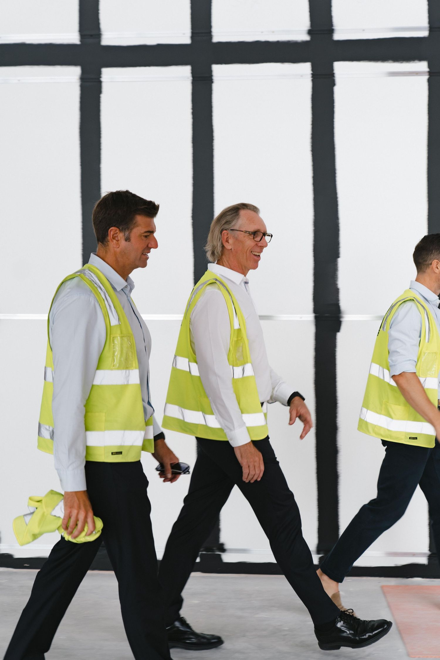 Workers in yellow safety vests walking through a modern building with geometric window patterns.