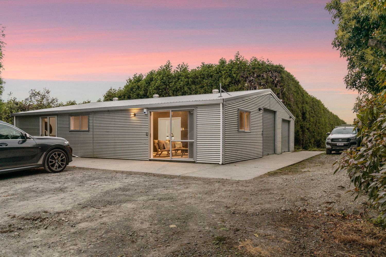 Exterior views of a modern gray home at sunset against a pink and purple sky.