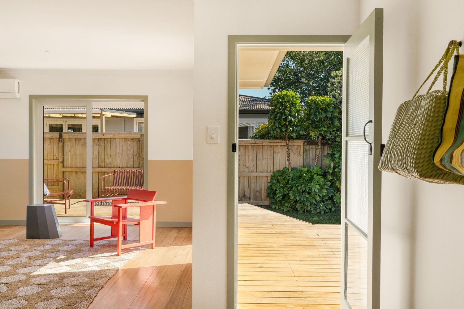 Interior doorway leading to wooden deck with view of red chair and garden fence through glass sliding door.
