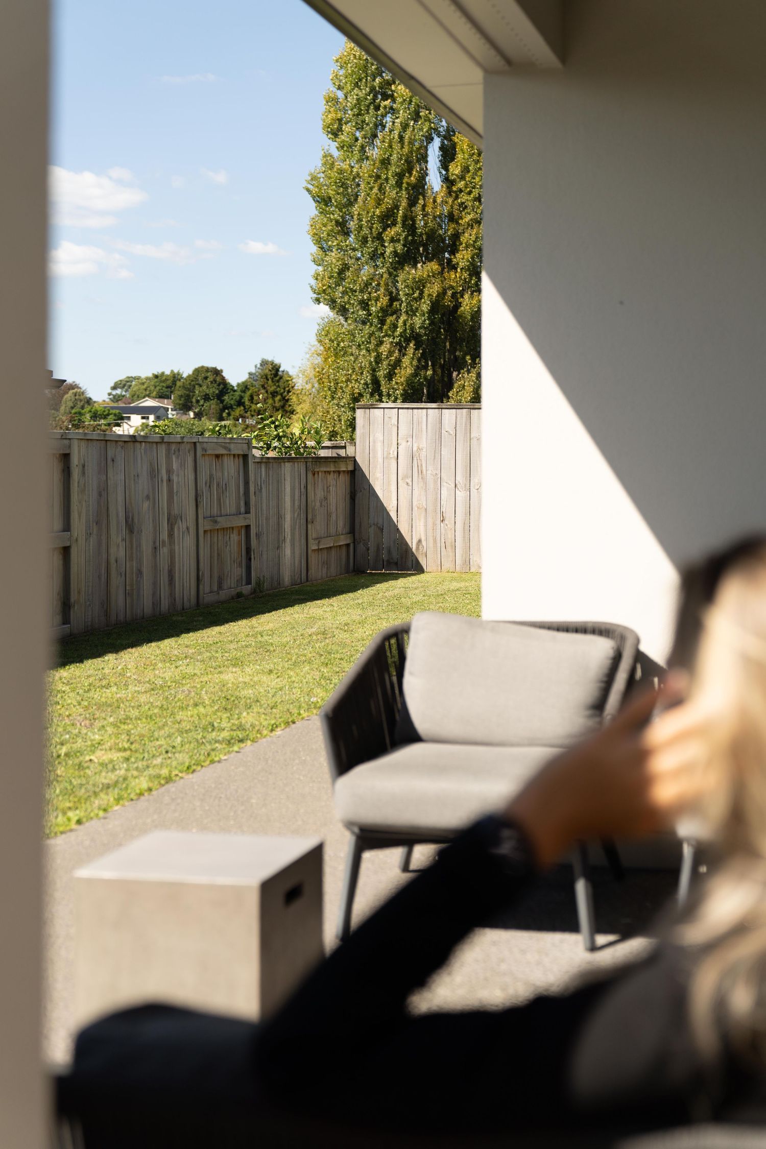A cozy outdoor patio setting with grey furniture and a wooden fence backdrop on a sunny day.