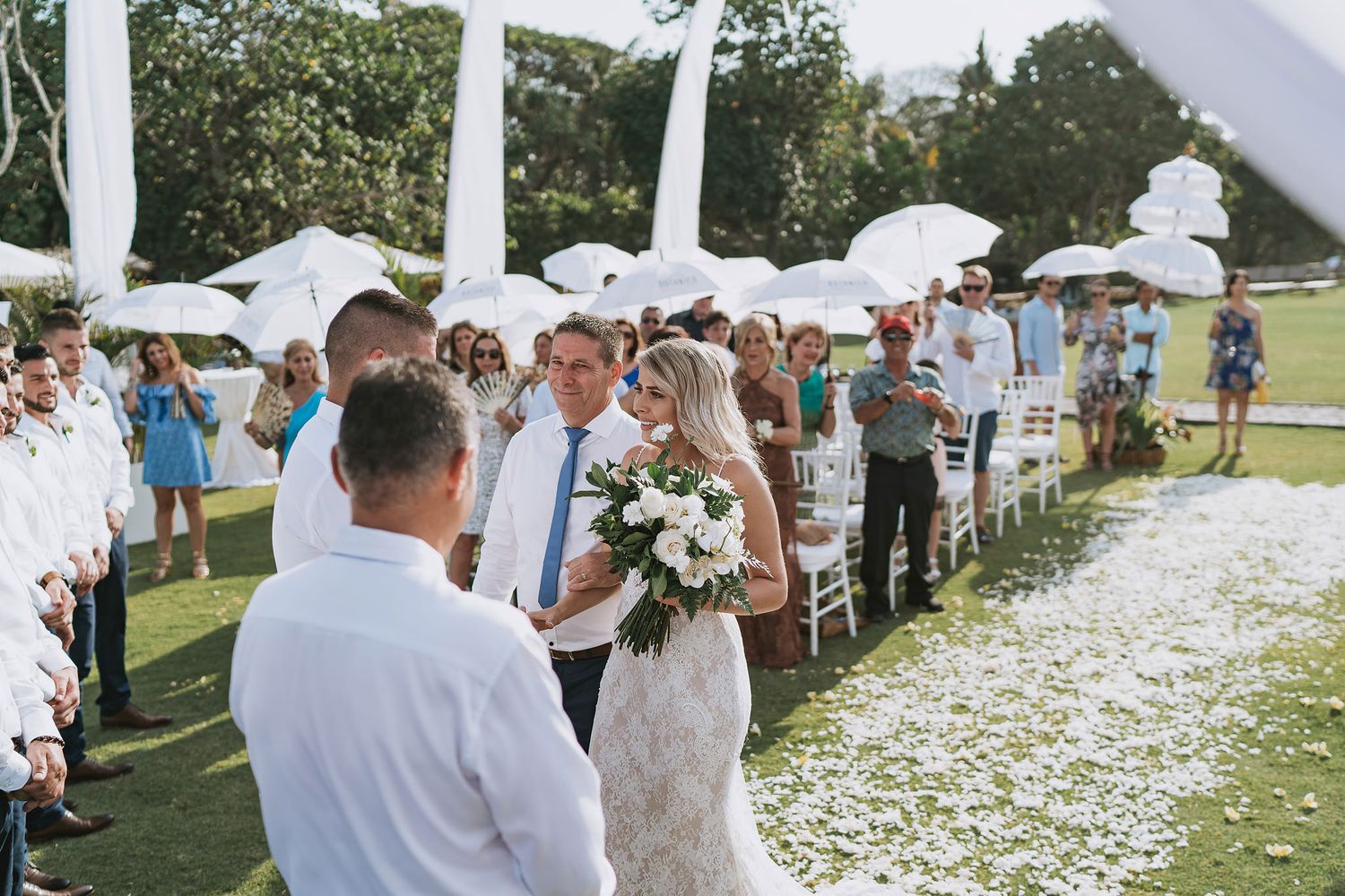 Wedding ceremony on lawn with white decorations and flower petals scattered along aisle.