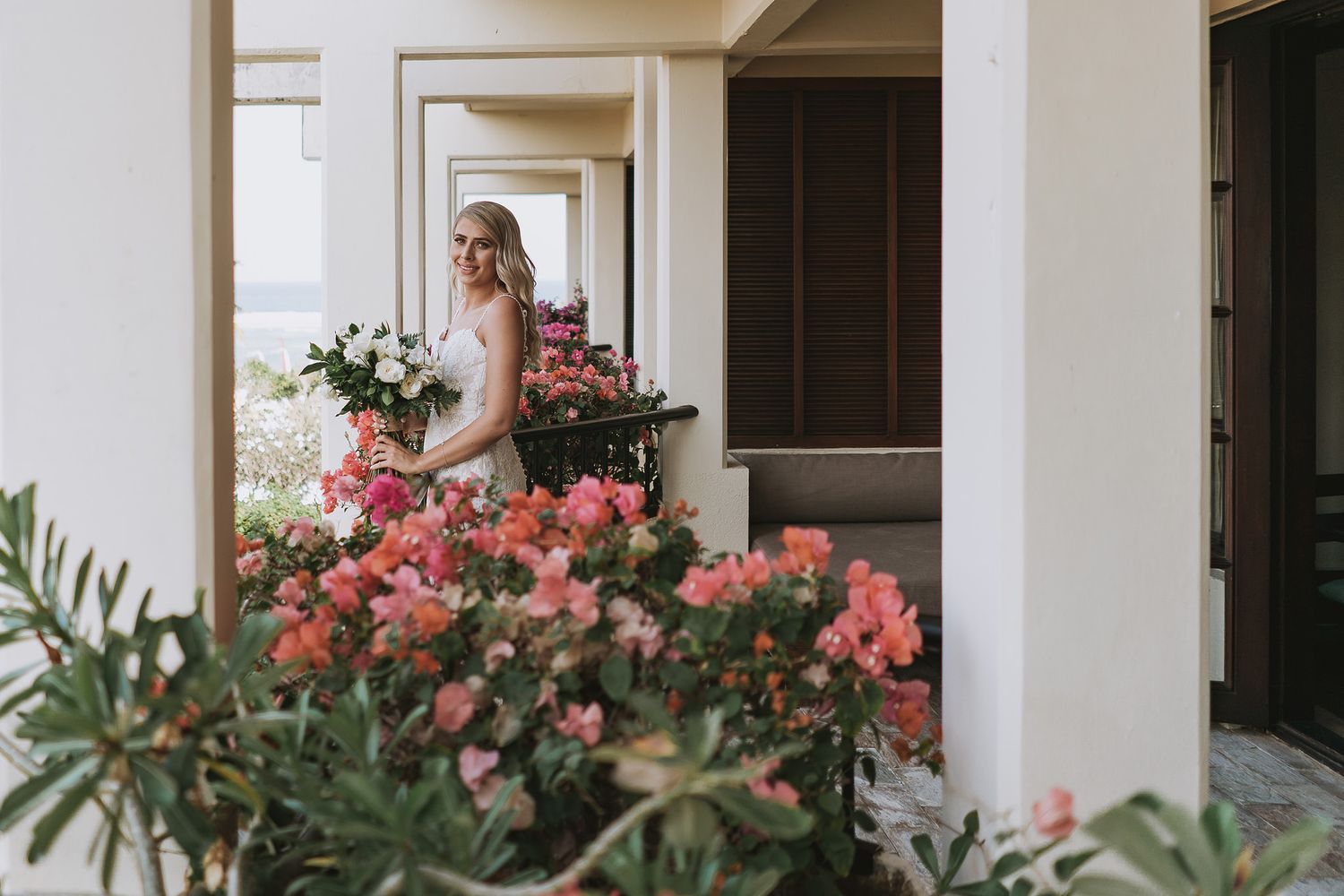 Person in white dress standing by doorway with pink flowers and greenery.