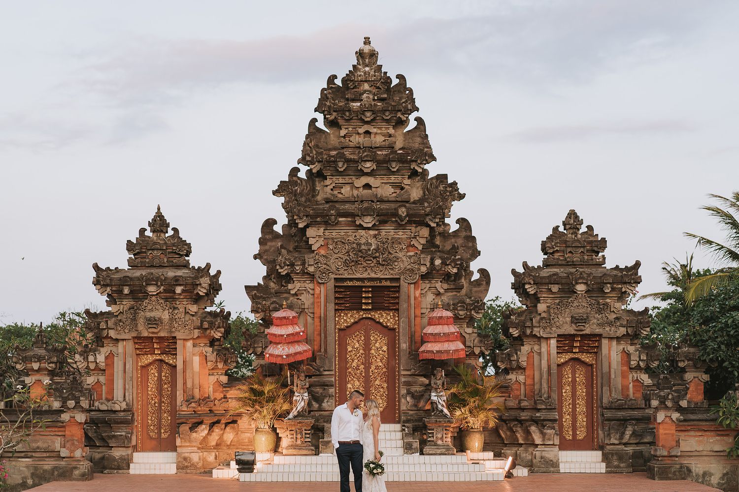 Couple stands before an ornate Balinese temple entrance with traditional architecture.