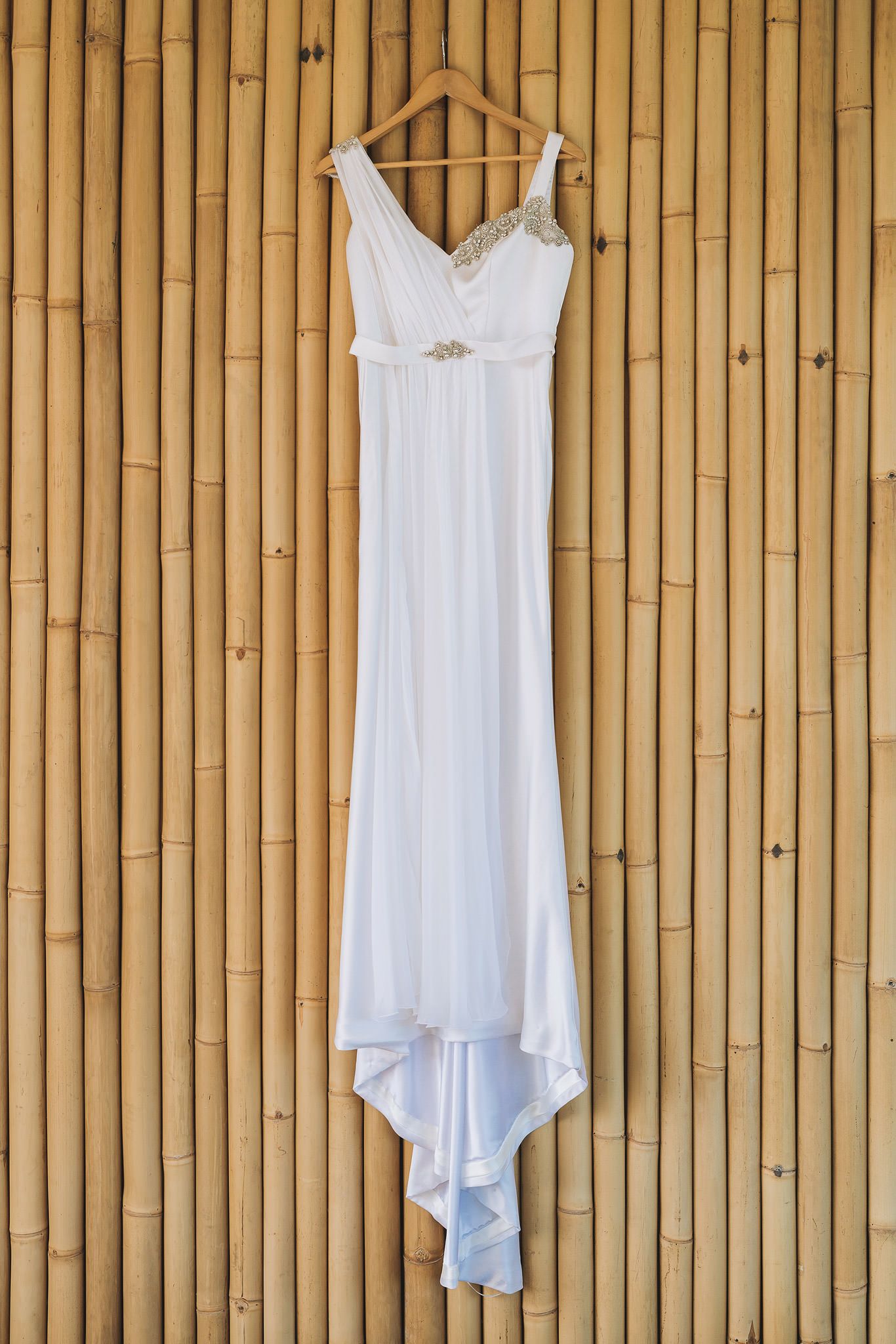 Three white summer dresses hanging on wooden slat wall display against natural bamboo backdrop.