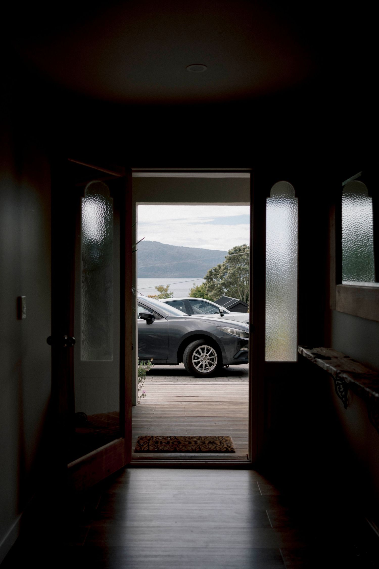Dark interior hallway with sunlight streaming through windows at the far end showing parked cars outside.