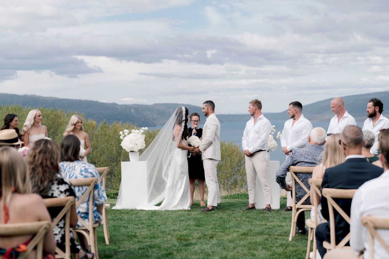 An intimate outdoor wedding ceremony takes place on a grassy hilltop overlooking scenic mountain views.