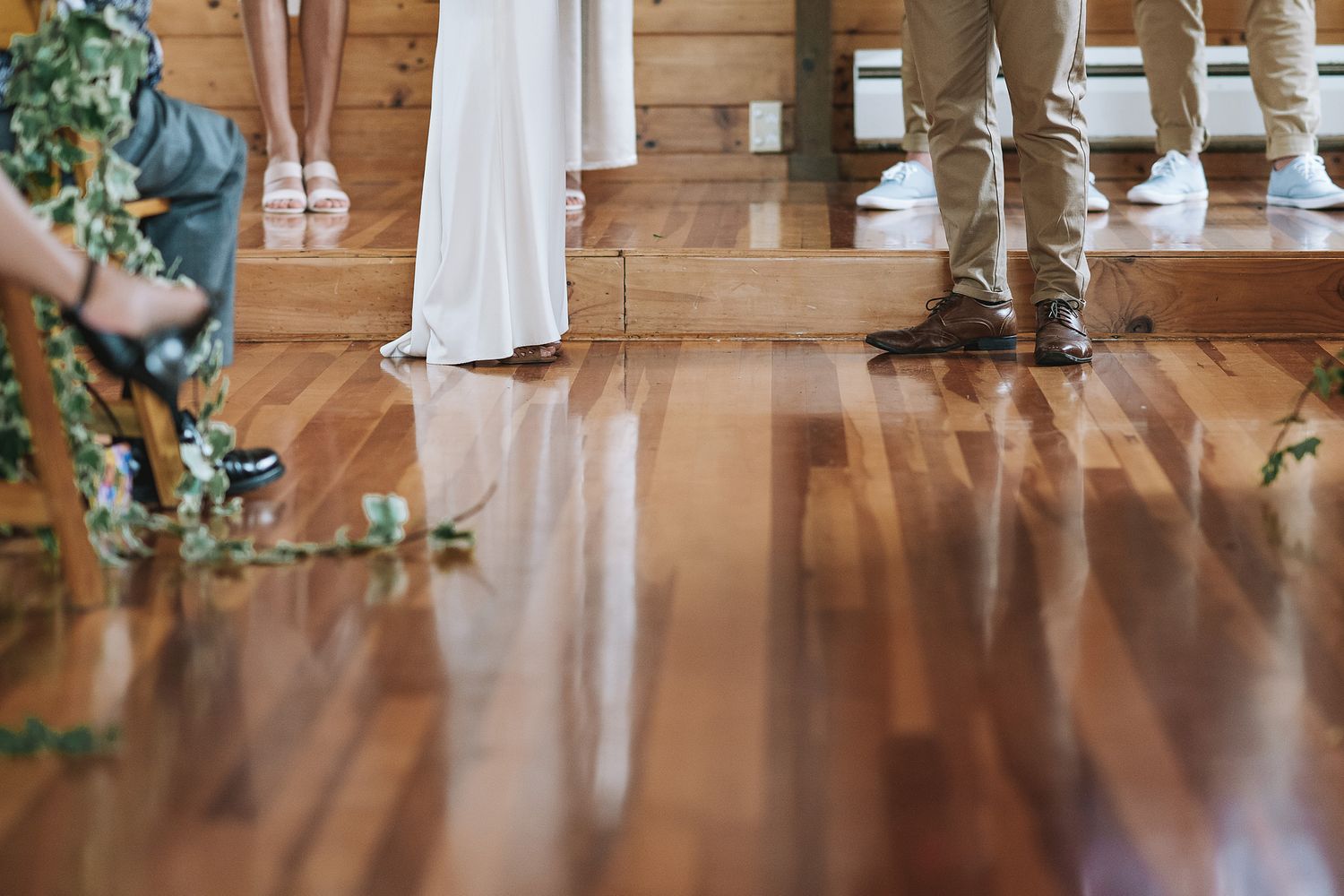 Close-up view of a polished hardwood floor with people standing in formal attire at what appears to be a wedding ceremony.