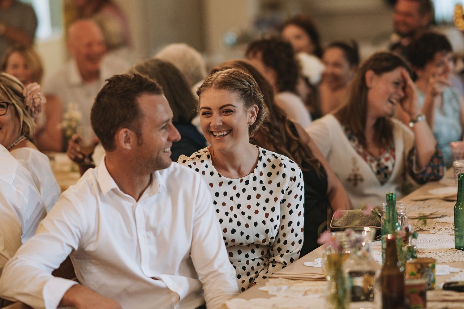 Dinner party guests share laughter around a table with wine glasses and warm lighting during a celebratory meal.
