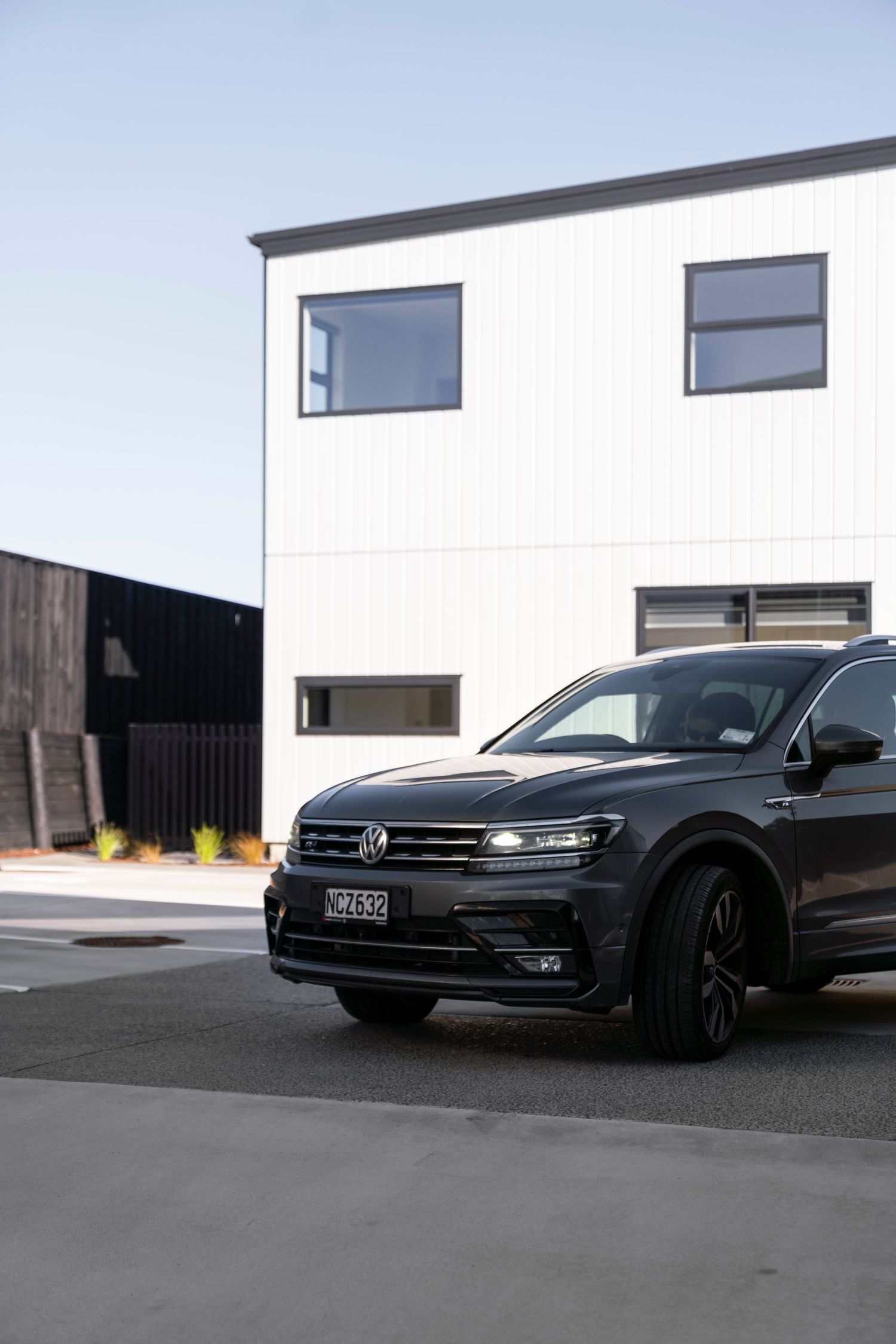 Black Volkswagen SUV parked in front of modern white and black architectural building.