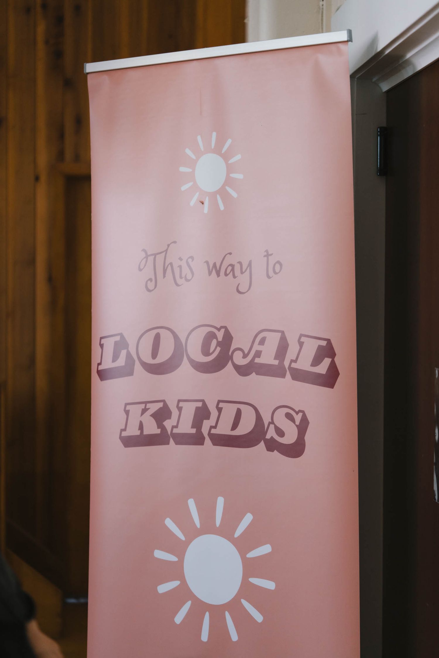 A pink banner display with 'This way to Local Kids' text and sun icons.