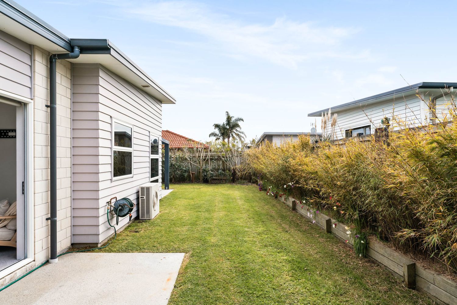 Modern suburban home exterior with well-maintained lawn and palm tree in the background under blue sky.