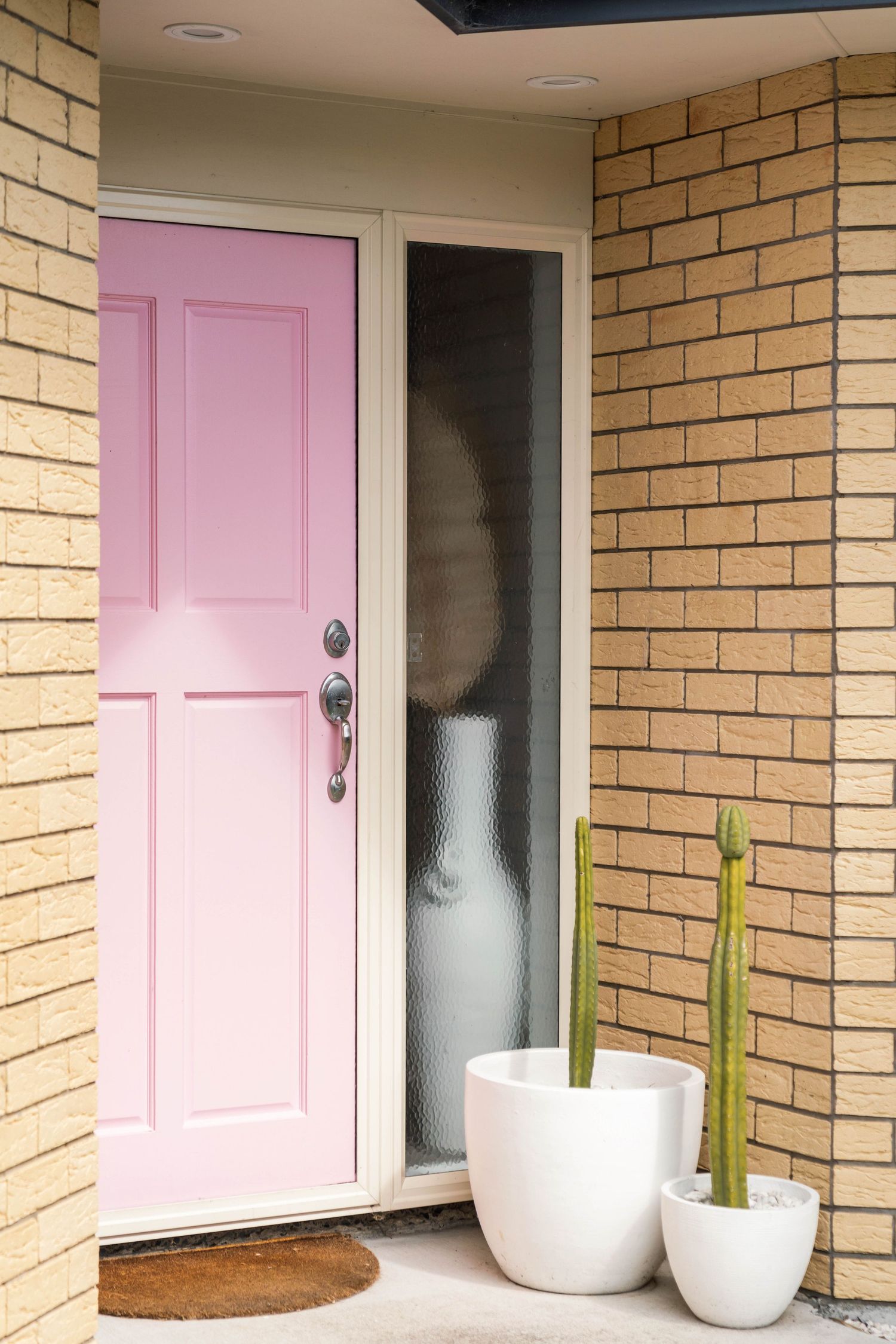 A pink front door with two white potted plants on a brick exterior entryway.