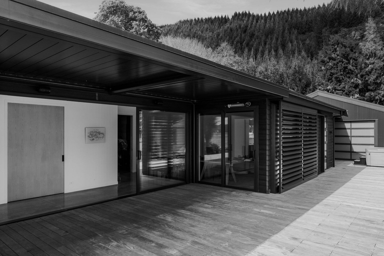 Modern minimalist house exterior features dark horizontal siding and floor-to-ceiling windows nestled in a forested setting.