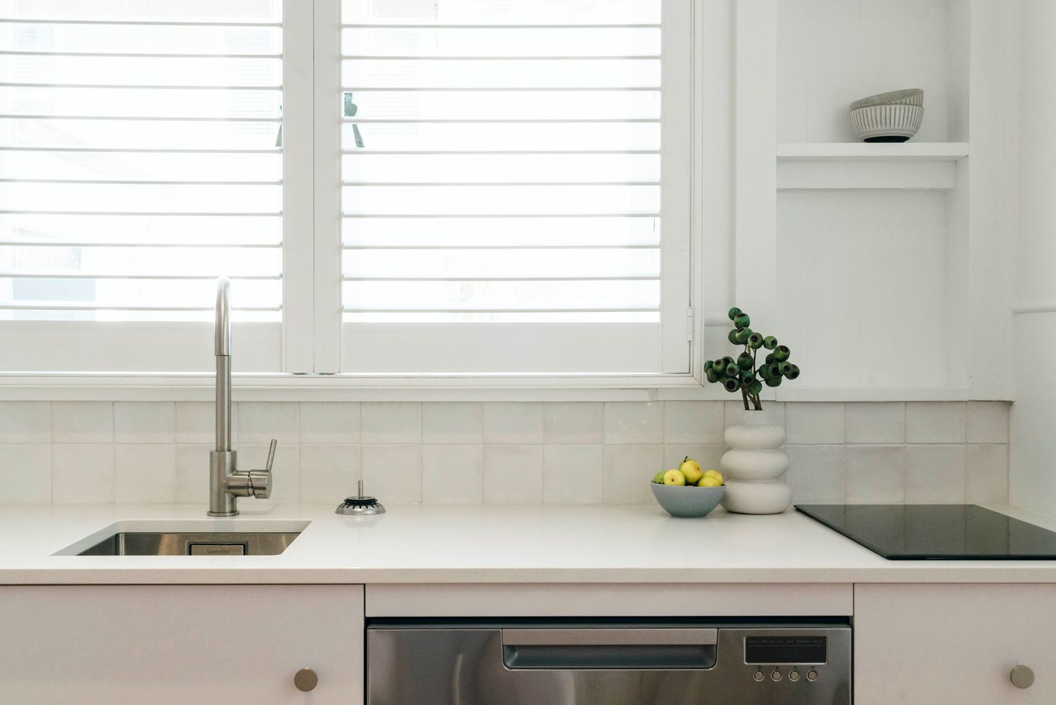 White modern kitchen with plantation shutters and integrated appliances.