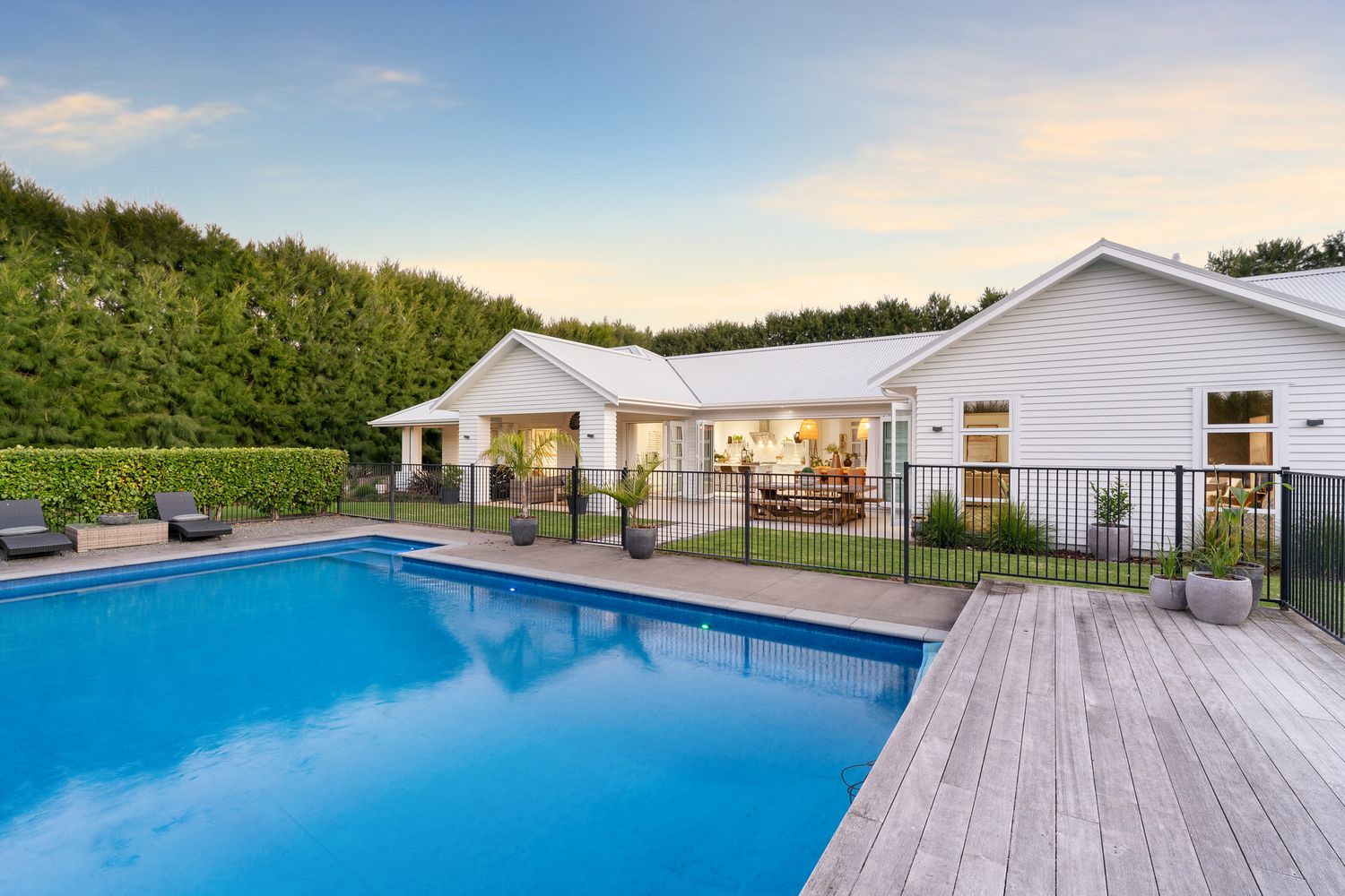 White modern farmhouse with pool deck and outdoor entertaining area at dusk.
