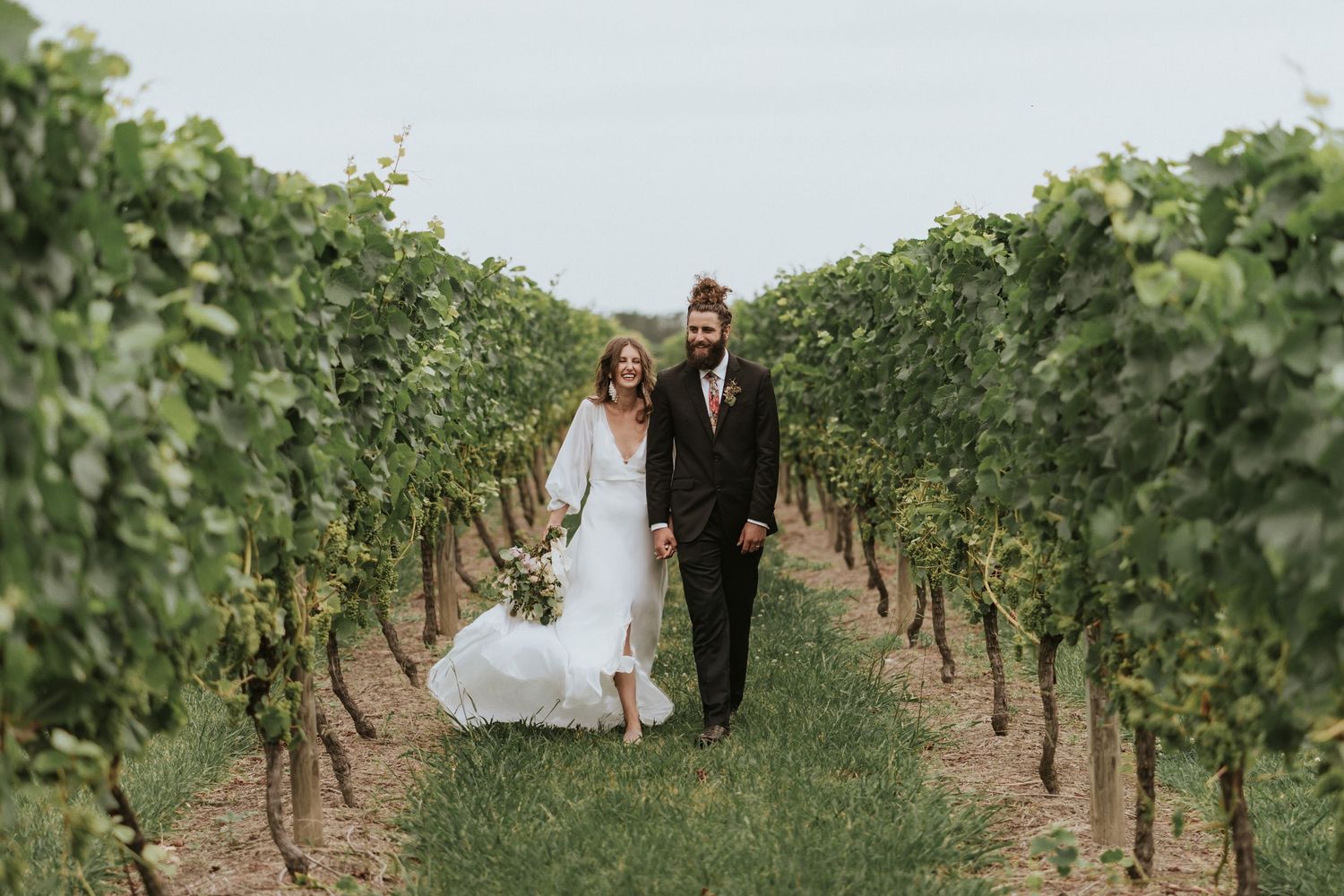 A couple walking together between rows of grapevines at a scenic vineyard on their wedding day.