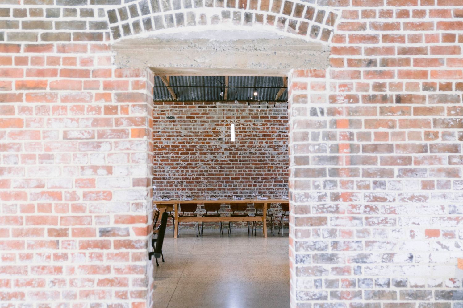 Rustic brick archway entrance with a wooden cross hanging in a historic building interior.