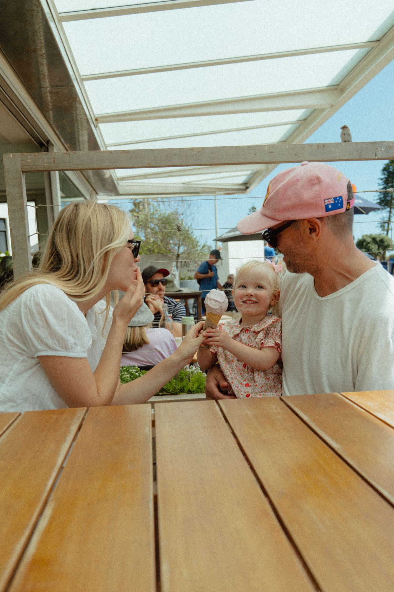 Family sharing ice cream cones at a wooden picnic table on a sunny day.