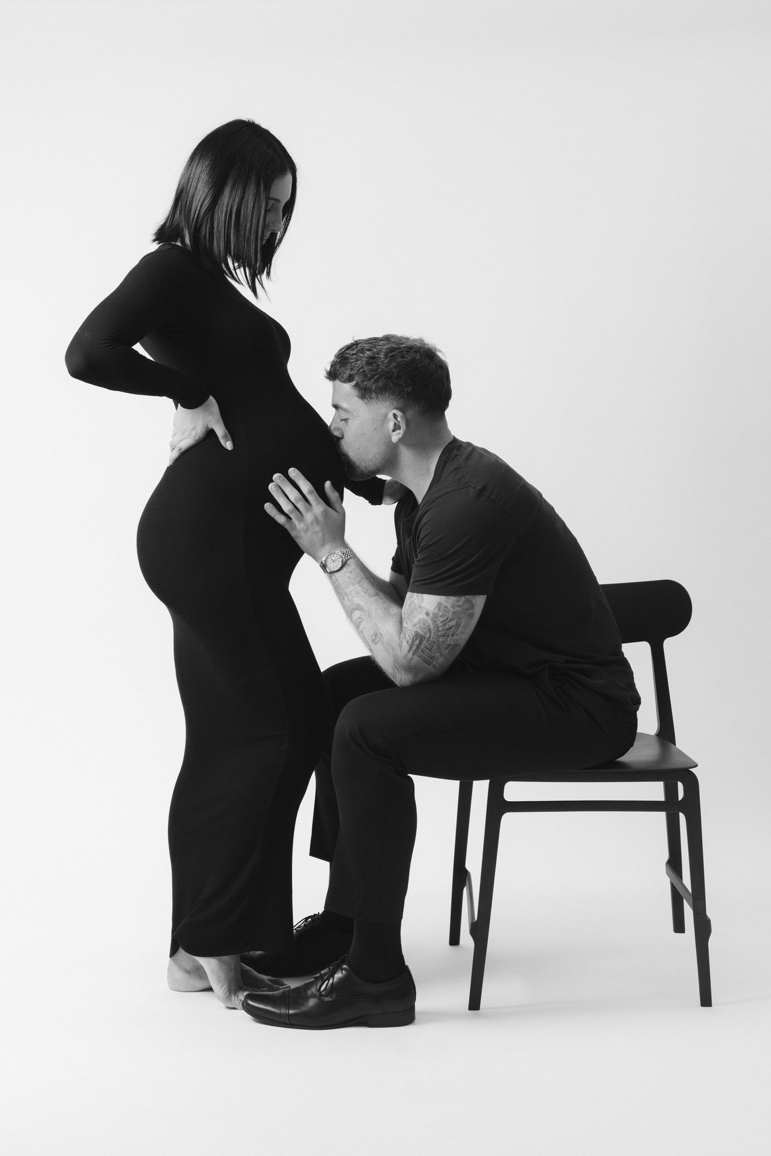 Three black and white artistic photographs showing figures in dark clothing interacting with chairs against a white backdrop.