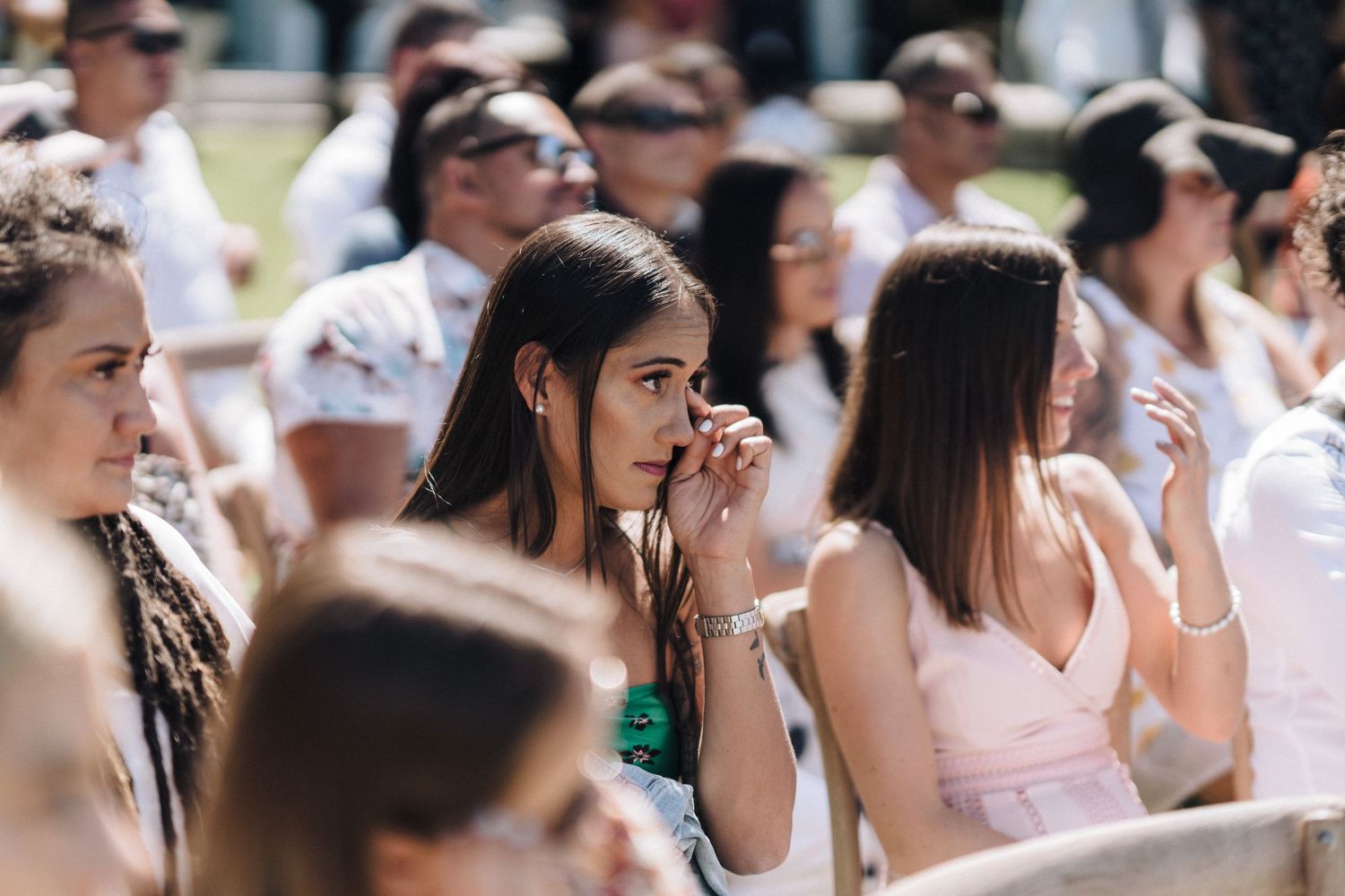 Group of wedding guests watching emotional ceremony outdoors on a bright summer day.