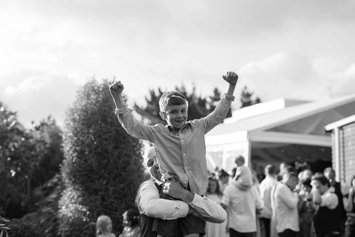 Joyful wedding celebration with dancing guests in formal attire on an outdoor patio during golden hour lighting.