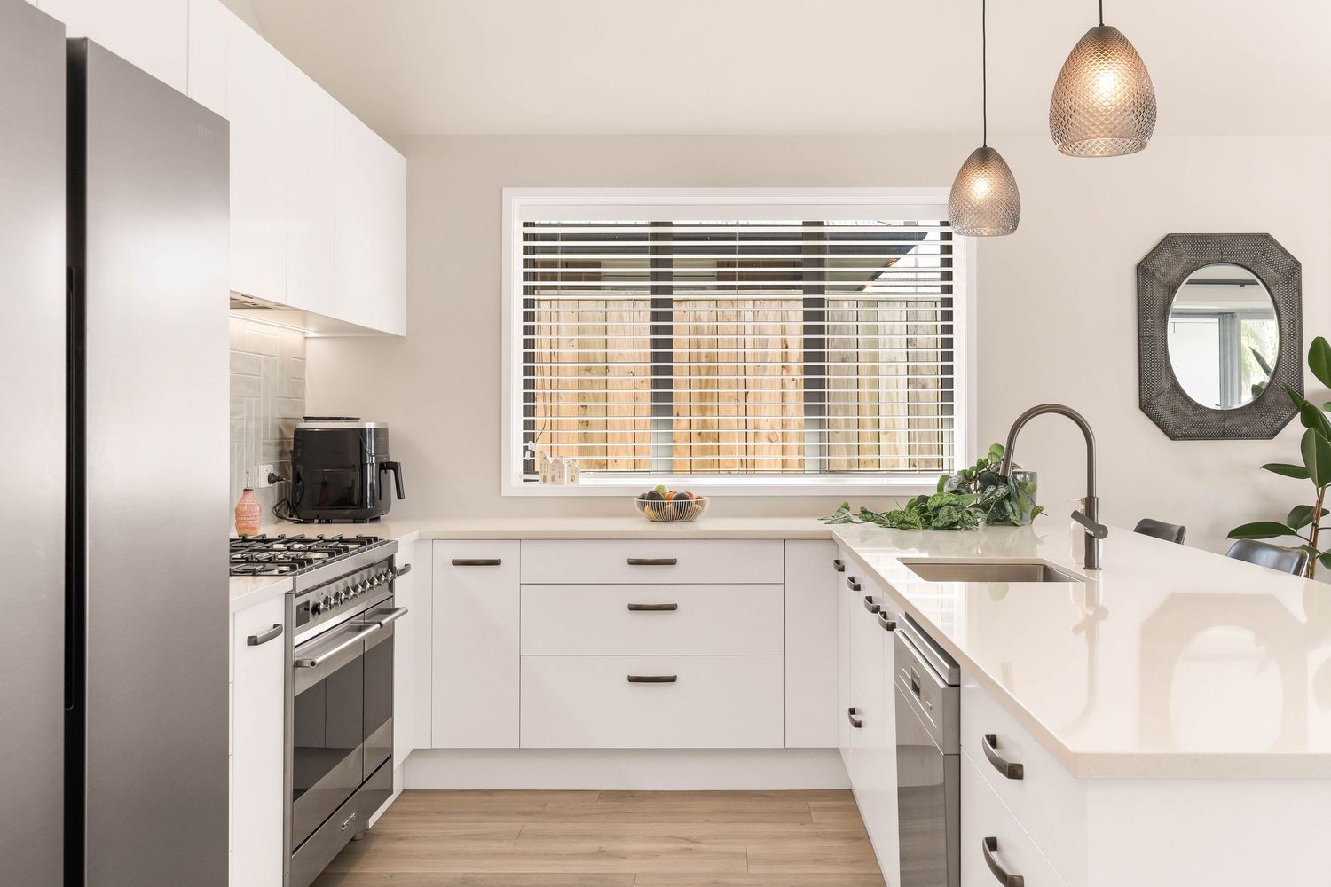 White L-shaped kitchen with stainless appliances, quartz countertops and modern cabinet hardware.