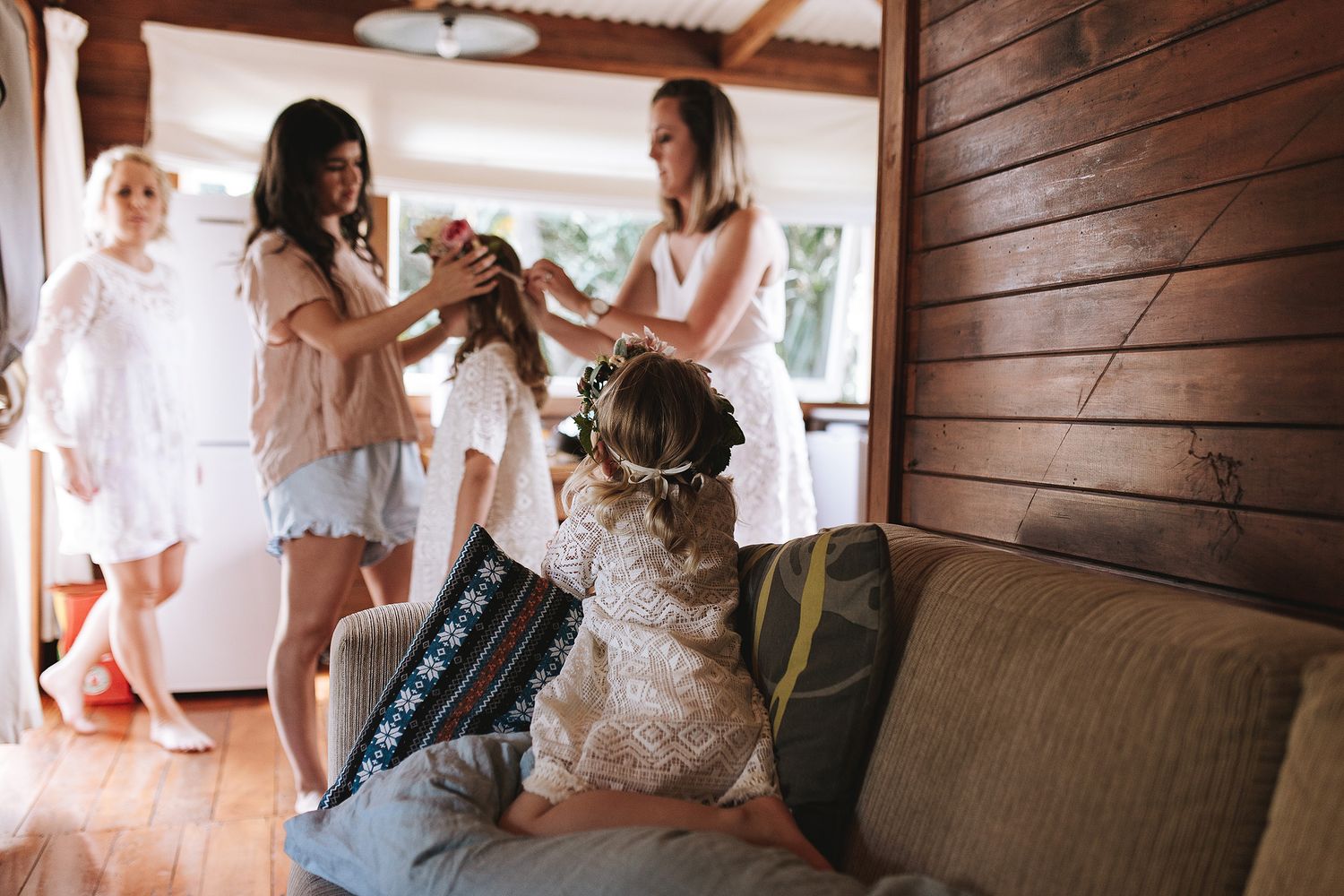 Wedding party members in white robes help with preparations in a wooden-paneled room.
