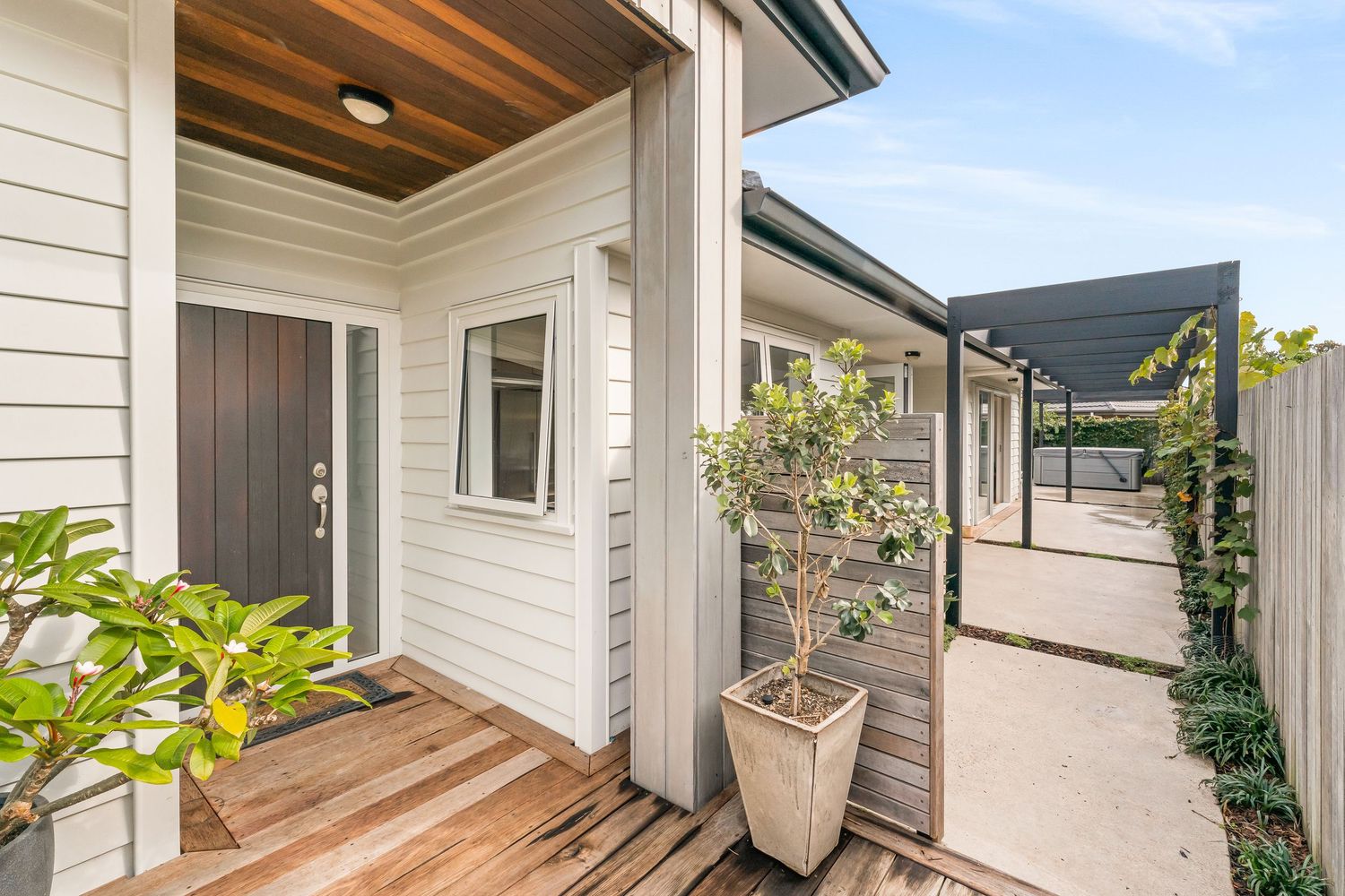 Contemporary home exterior with weatherboard siding, covered porch and potted plants along walkway.