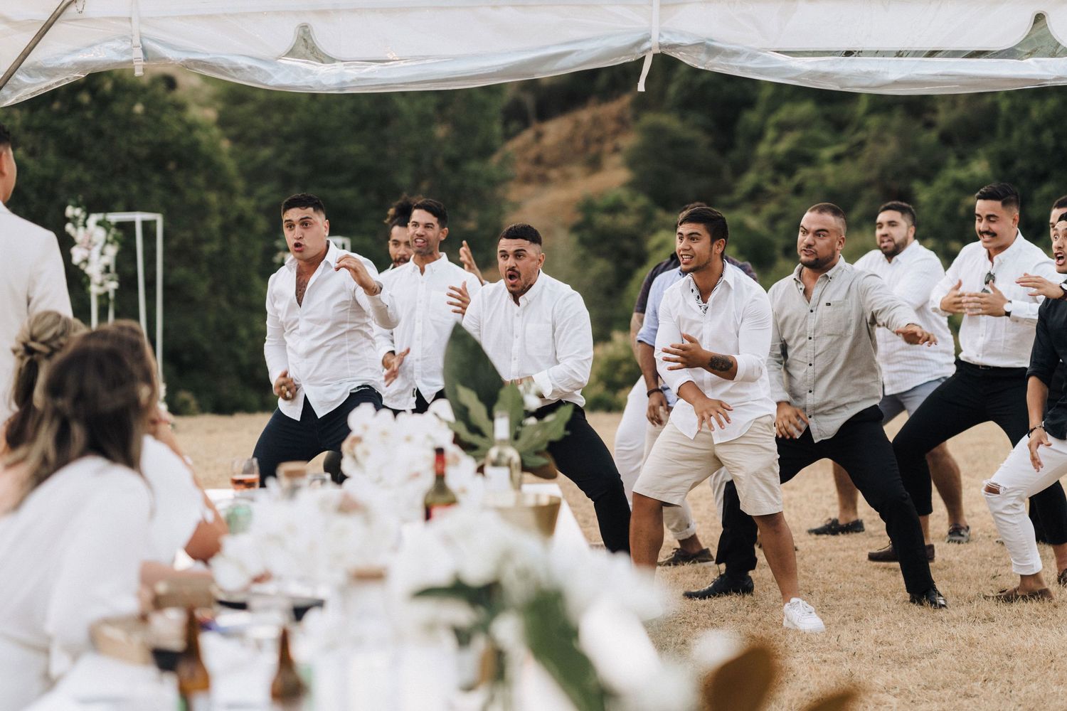 Group of groomsmen in white shirts performing dance routine at outdoor wedding reception.