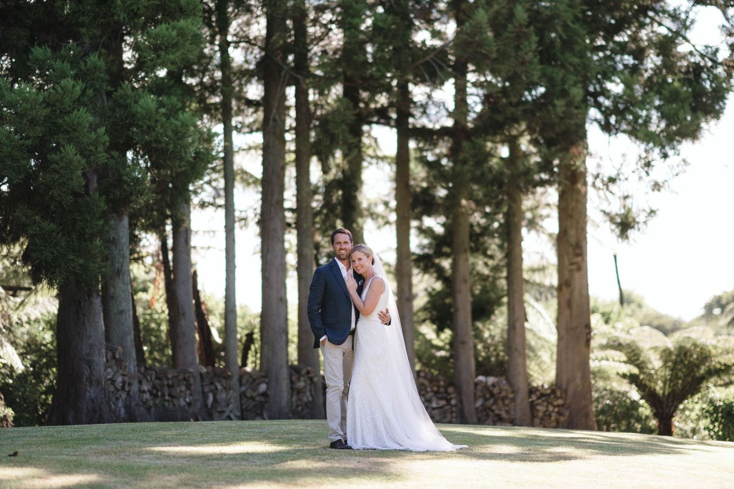 Wedding couple embracing on hilltop surrounded by tall pine trees.