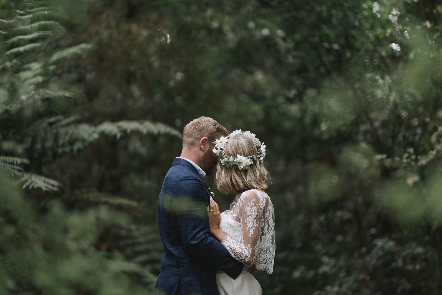 A newlywed couple embraces intimately amidst a verdant forest backdrop on their wedding day.