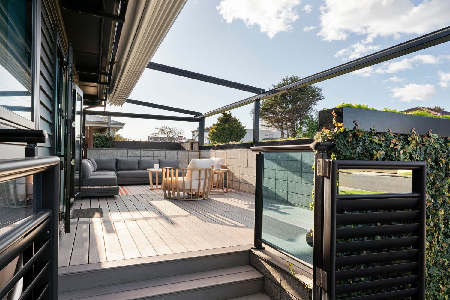 Modern deck with glass balustrade and outdoor furniture under a contemporary pergola structure.
