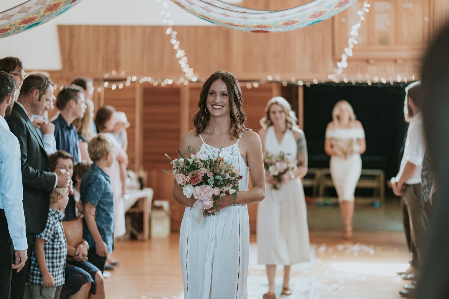 String light decorations illuminate a rustic wooden barn venue during a wedding celebration with guests mingling.