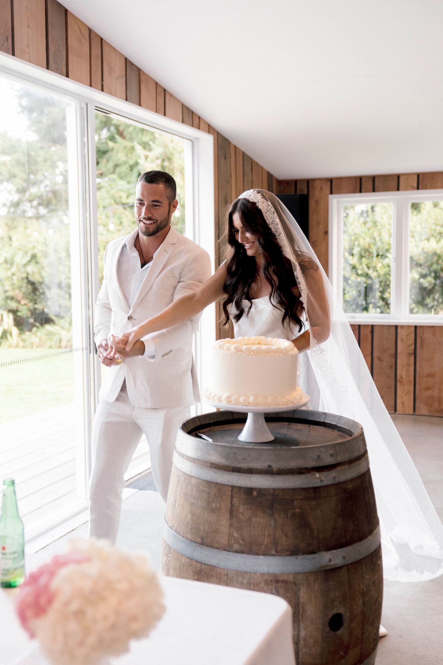 A couple laughing and celebrating around wine barrels in a rustic indoor venue.