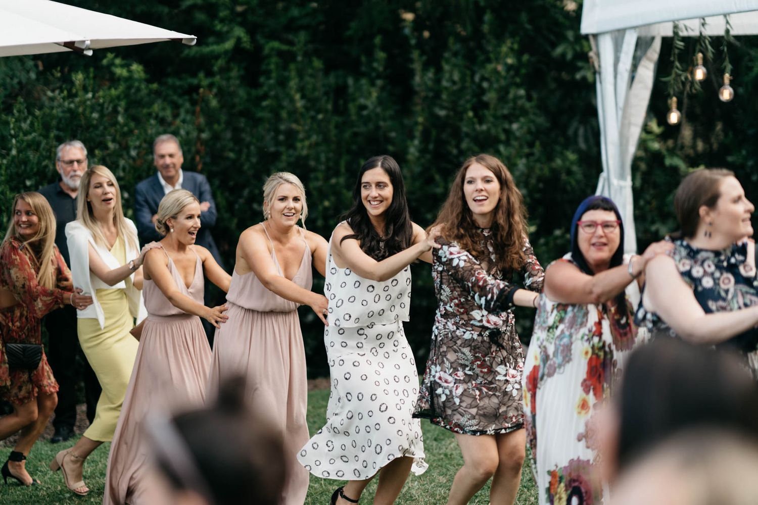 A group of guests dancing outdoors under white tents at a garden party celebration.