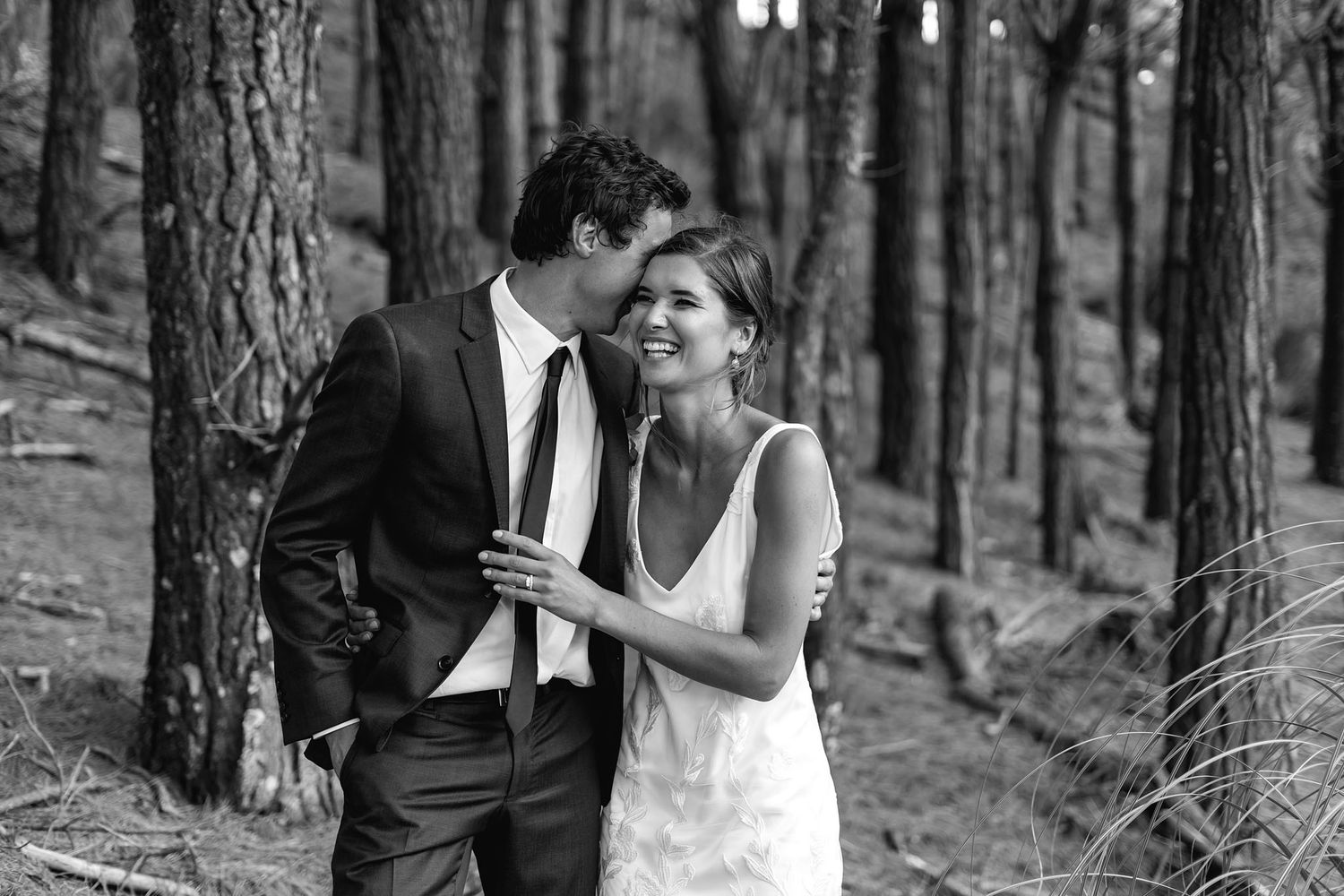A couple embraces in a serene forest setting during a wedding photoshoot among tall pine trees.