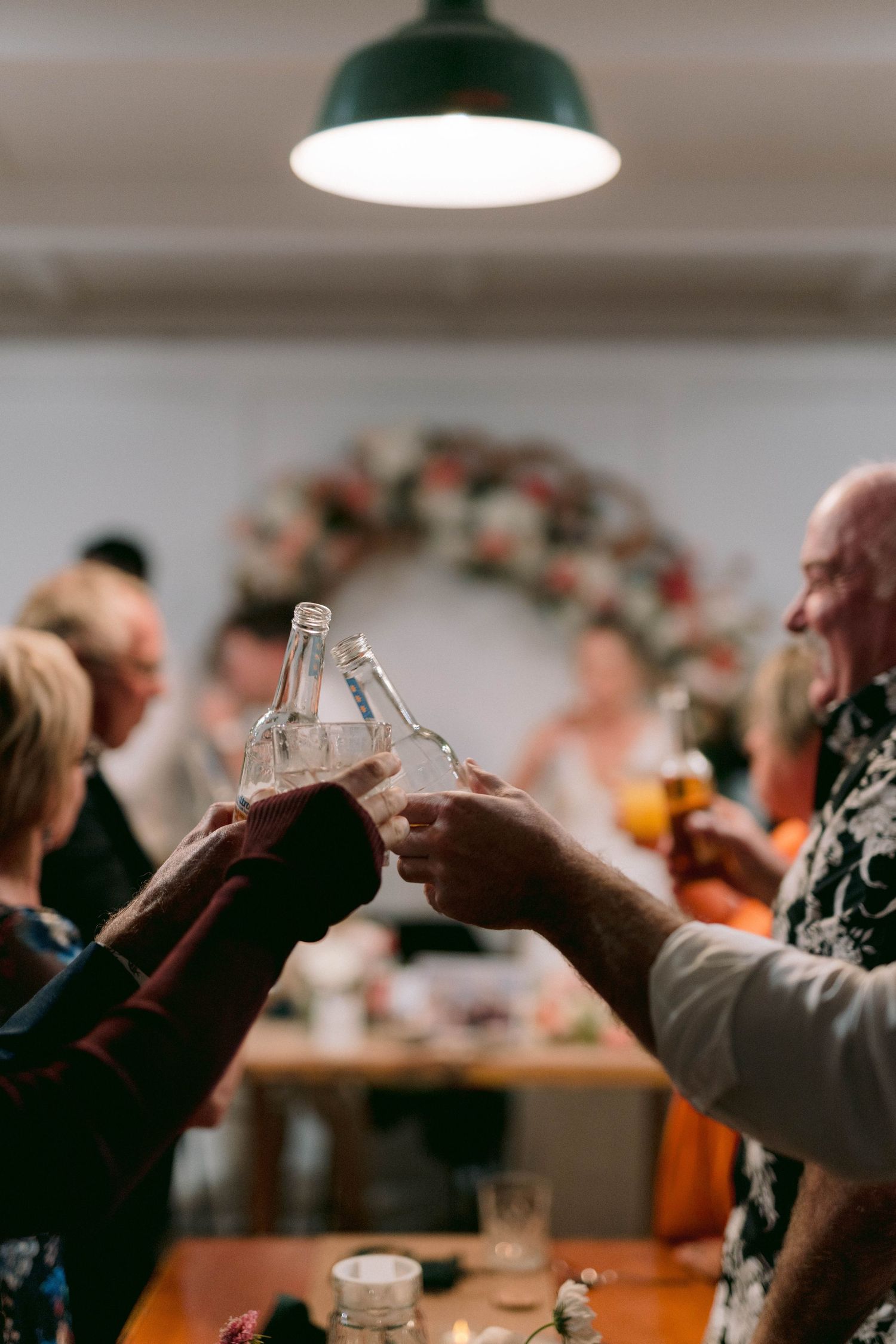 Wedding guests toasting with glasses under pendant lighting and floral decor.