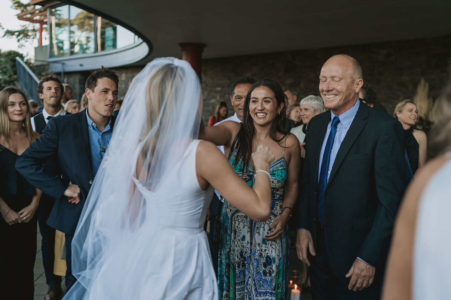A bride in a white dress and veil mingles with wedding guests during a reception celebration.