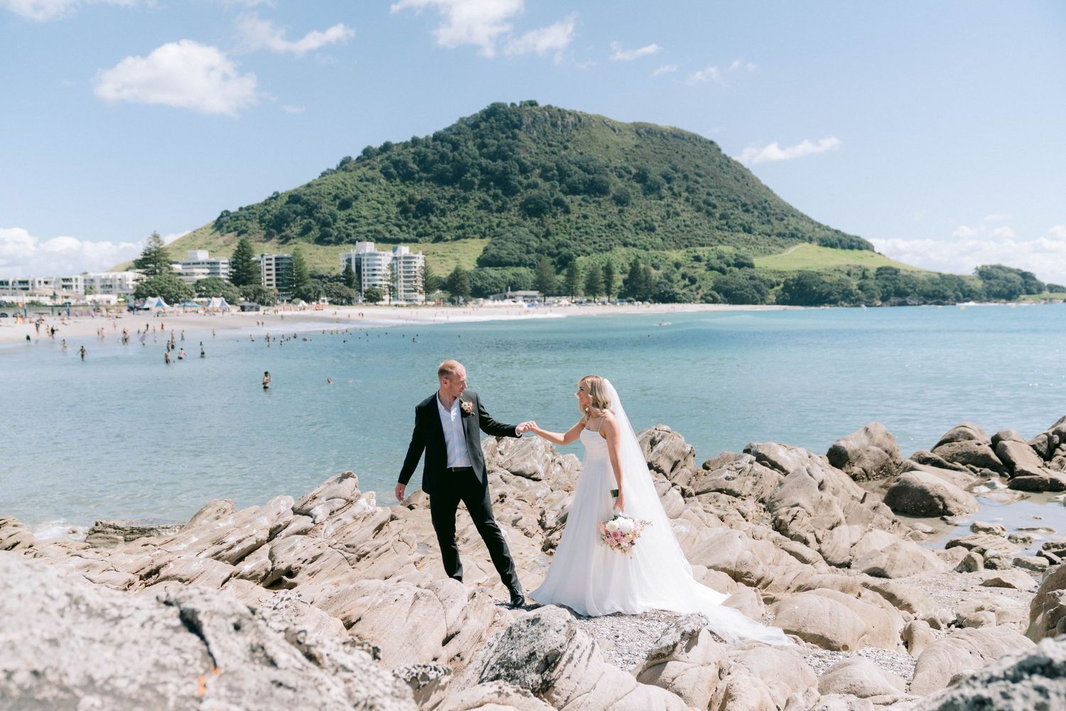 Beachside wedding portraits with mountain views and rocky shoreline in the background.