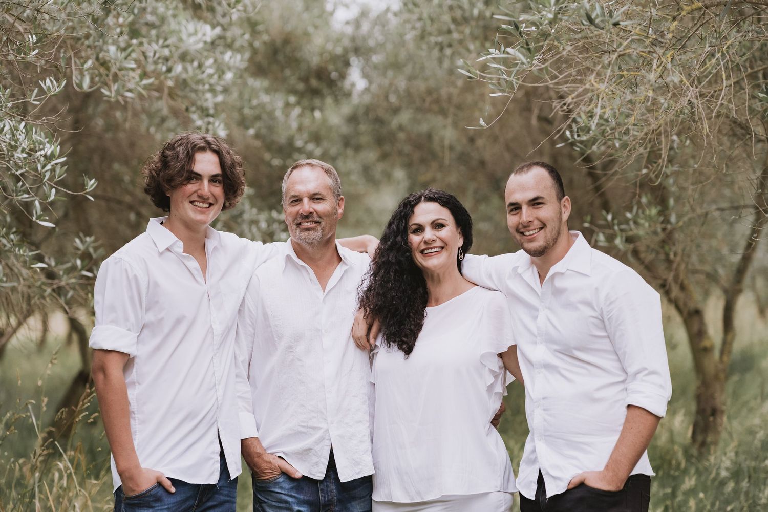 A group in white clothing poses together for casual outdoor photos in a natural wooded setting.