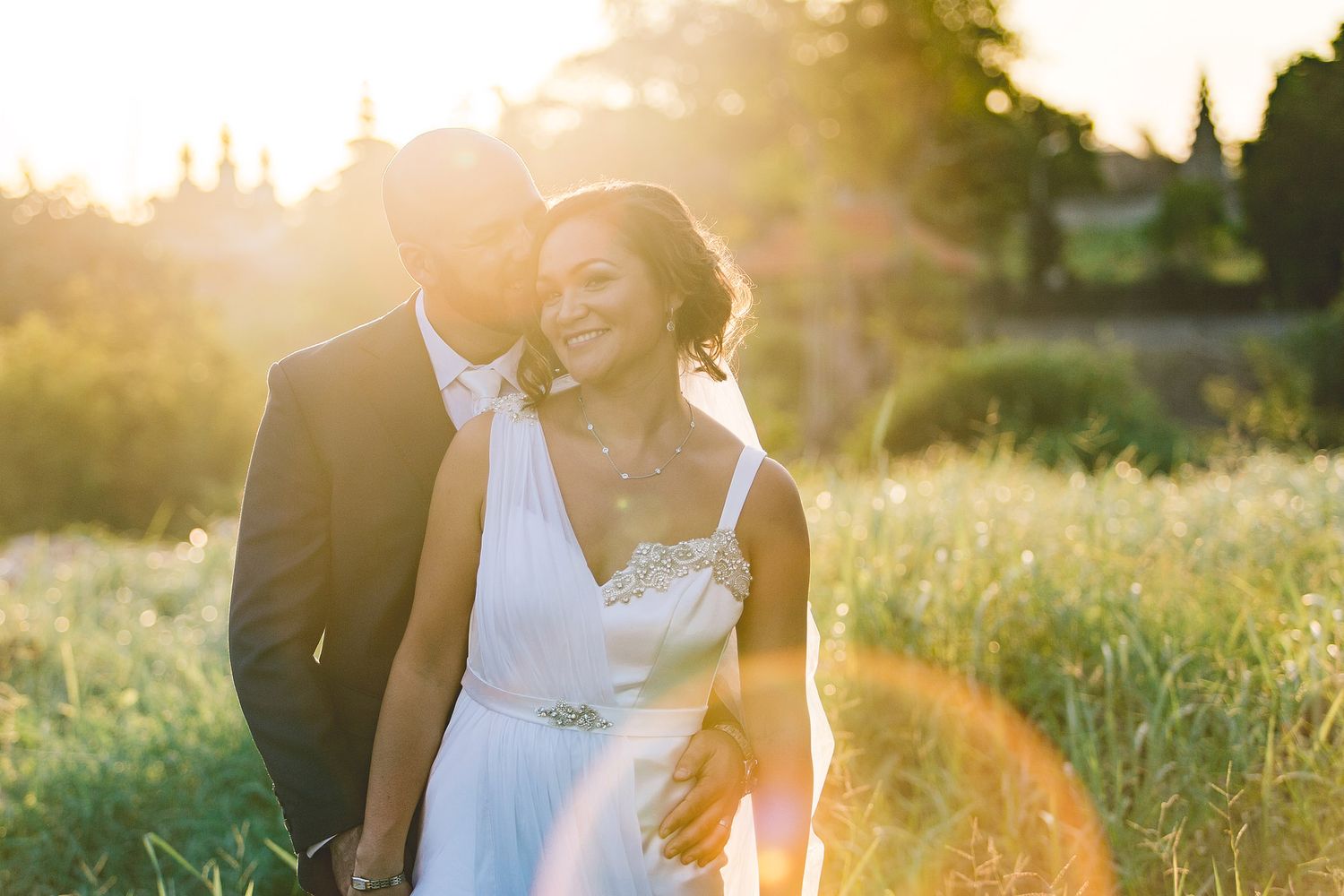 Golden hour portrait of couple in wedding attire in sunlit field.