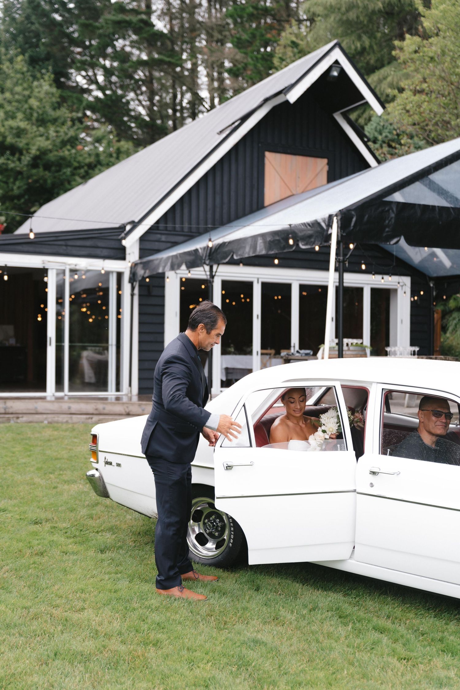 A classic white vintage car parked outside a modern black barn-style venue.