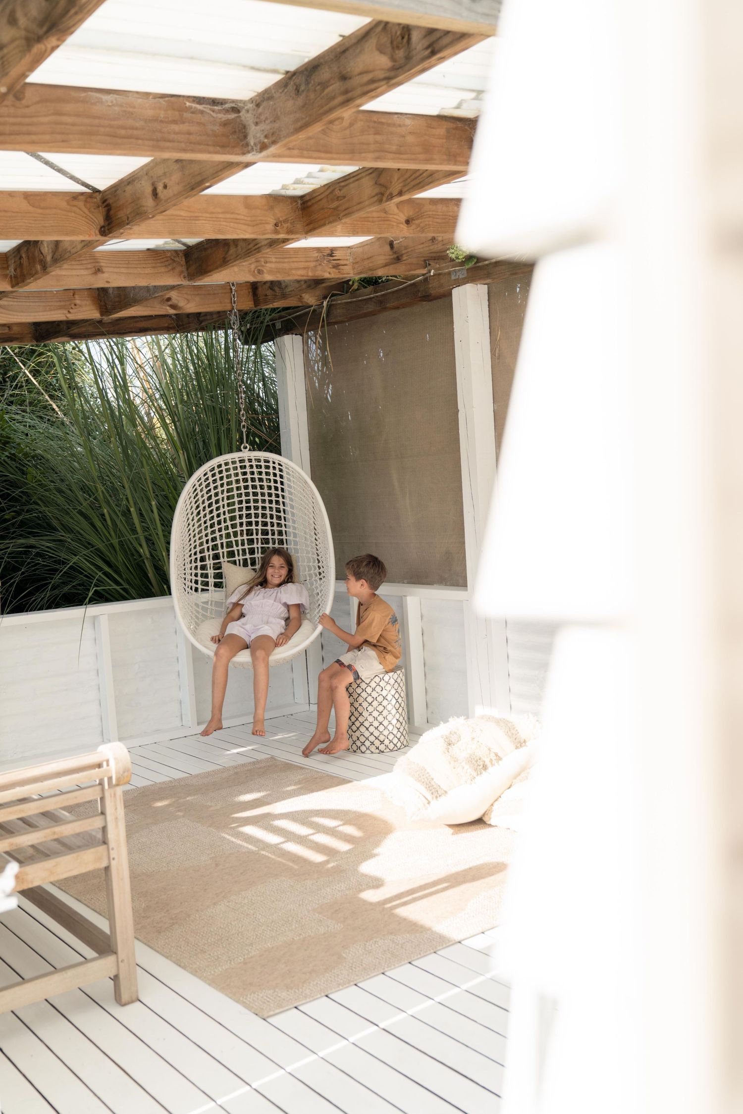 Two chairs on a white wooden deck with exposed wooden beams overhead create a cozy outdoor seating area.