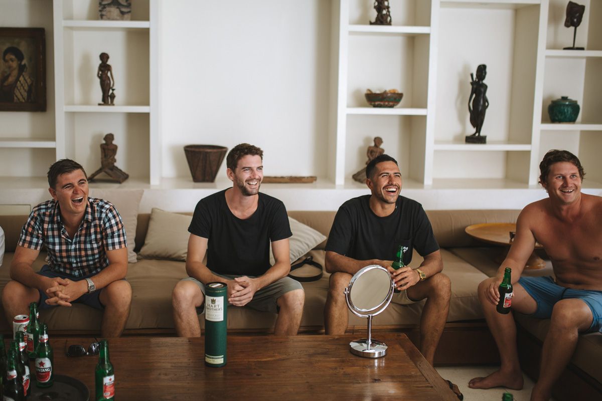 Group of friends relaxing on couch with drinks while having casual conversation in modern living room.